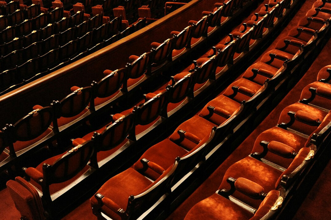 Empty theatre auditorium with rows of velvet seats facing an empty stage